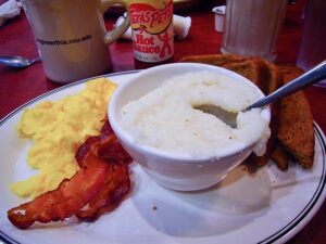 Picture of a typical Southern breakfast featuring eggs, bacon, and a bowl of grits.