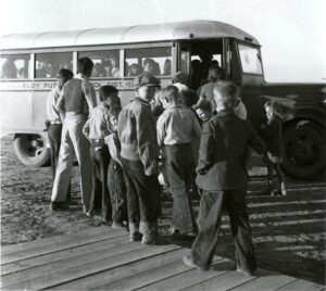Black and white picture of white children getting on a school bus in 1940.