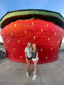 Picture of two young ladies standing out in front of the world's largest strawberry.